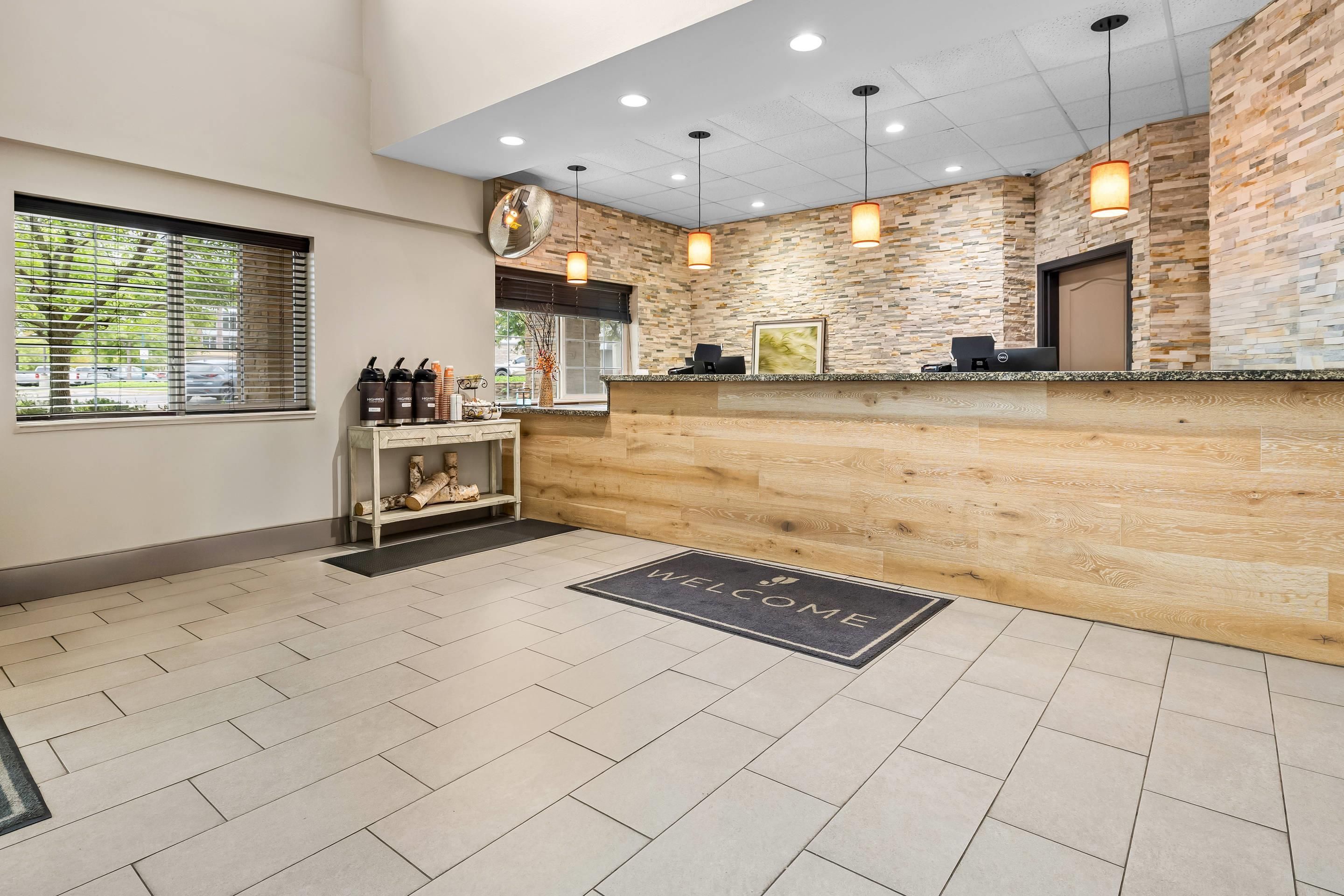 A reception area with a wooden reception desk, a welcome mat, and a view of the outside through a window with blinds.