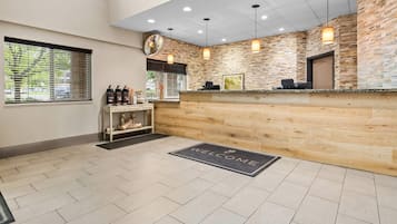 A reception area with a wooden reception desk, a welcome mat, and a view of the outside through a window with blinds.