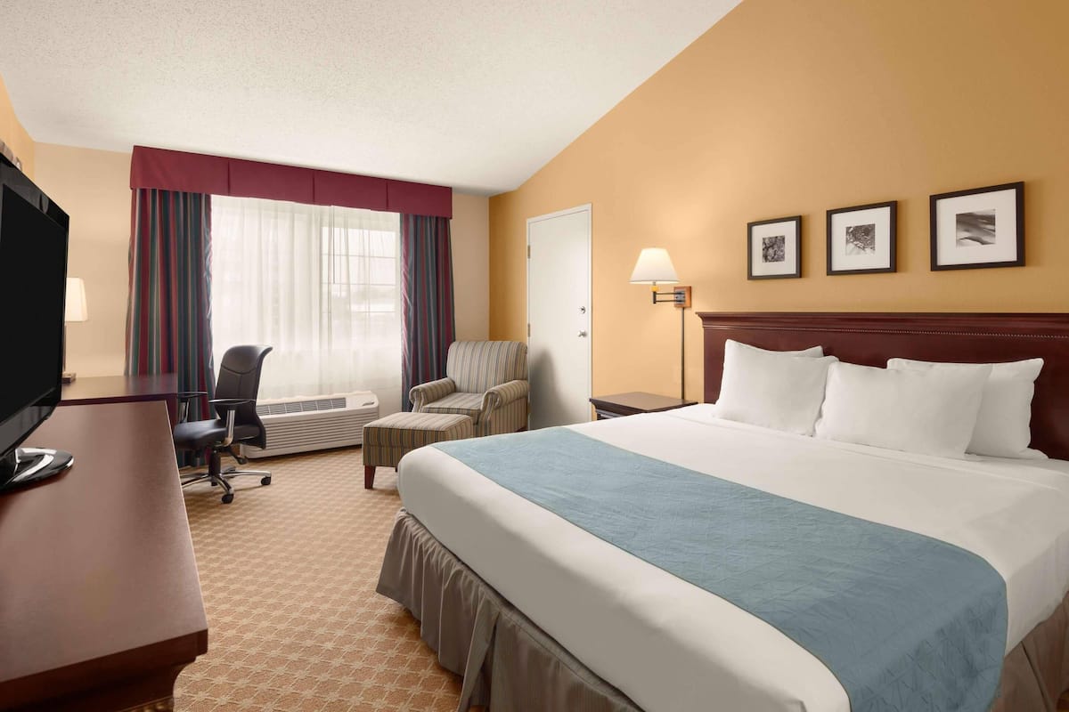 A hotel room with a large bed, a desk with a computer, a chair, a lamp, and three framed pictures on the wall.
