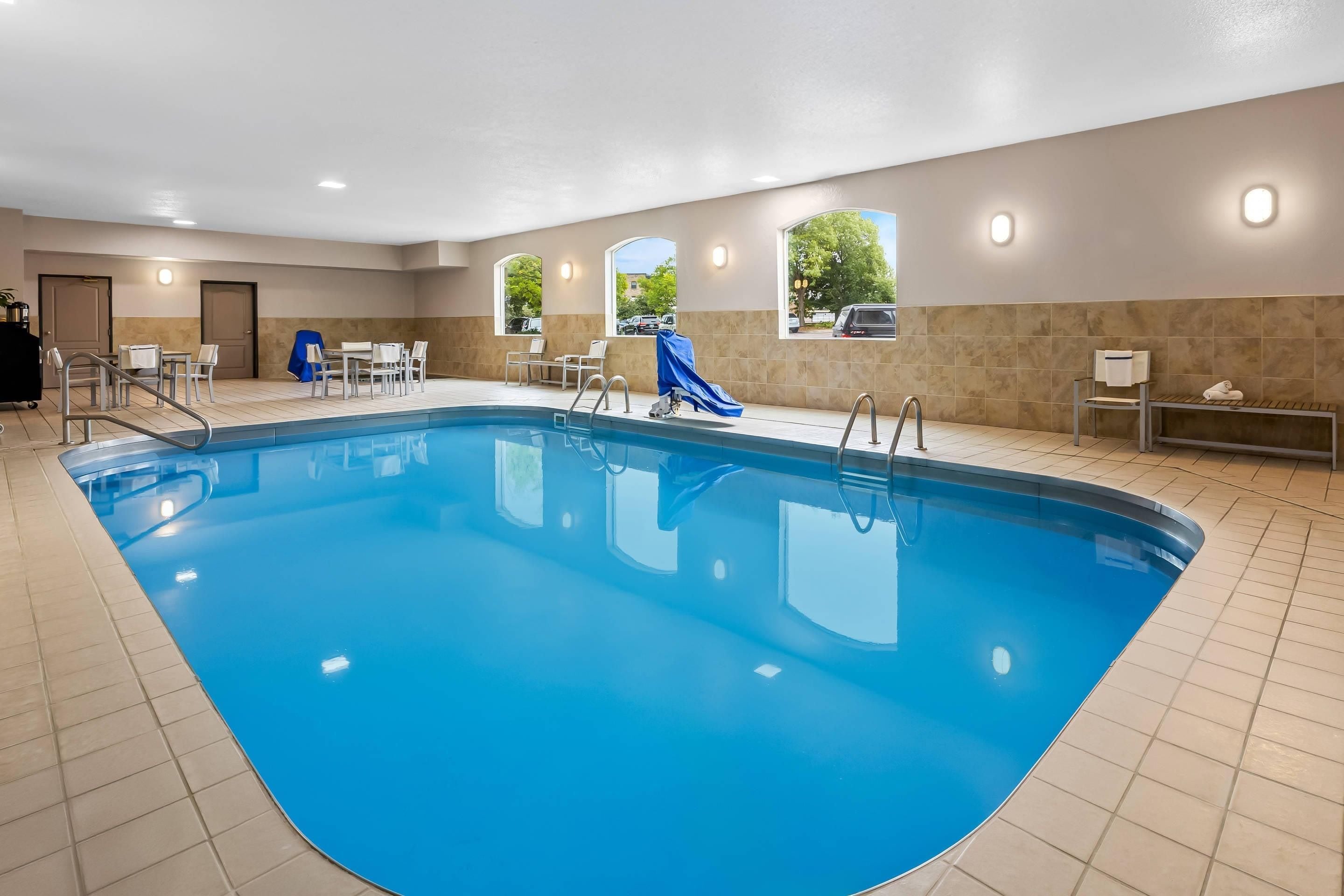 An indoor swimming pool with a blue color, surrounded by beige walls and a tiled floor.