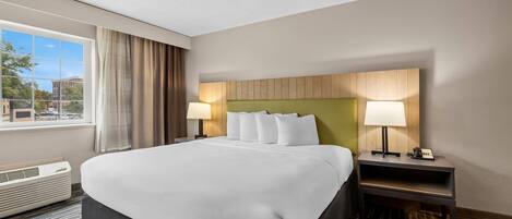 A hotel room with a large bed, two bedside tables with lamps, a window with curtains, and a view of the outside.