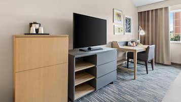A hotel room with a desk, a flat-screen TV, a wardrobe, and a bed with a headboard.