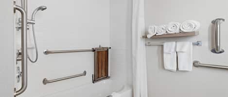 Une salle de bain avec une baignoire blanche, une douche avec un pommeau de douche amovible, un porte-serviettes avec des serviettes et une étagère en bois avec des serviettes pliées.