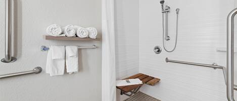 Une salle de bain moderne équipée d’une douche, de barres d’appui, d’un banc et d’un porte-serviettes où les serviettes sont soigneusement pliées.
