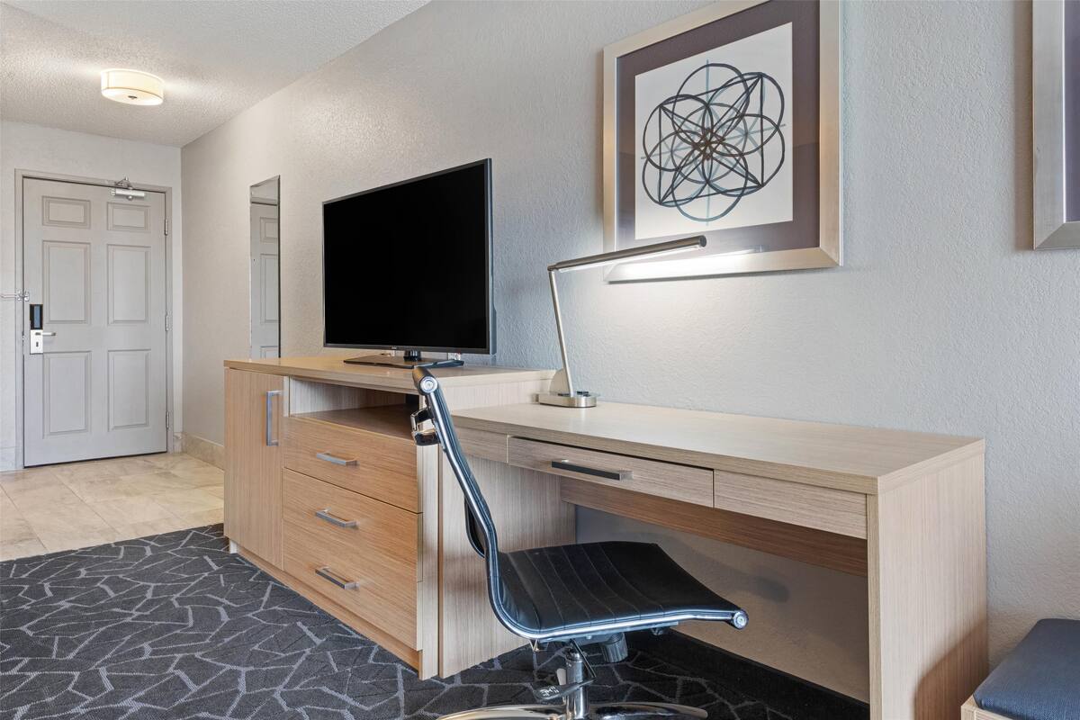 A modern office space with a desk, chair, television, and framed artwork on the wall.