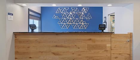 A reception desk with a geometric wall art, a digital check-in kiosk, and a wooden panel design.