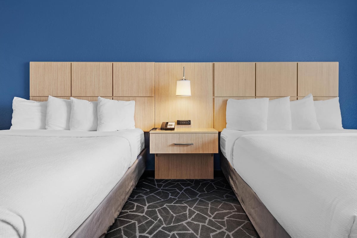 A hotel room with two beds, a wooden headboard, a bedside table with a lamp, and a patterned floor.