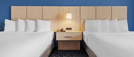 A hotel room with two beds, a wooden headboard, a bedside table with a lamp, and a patterned floor.