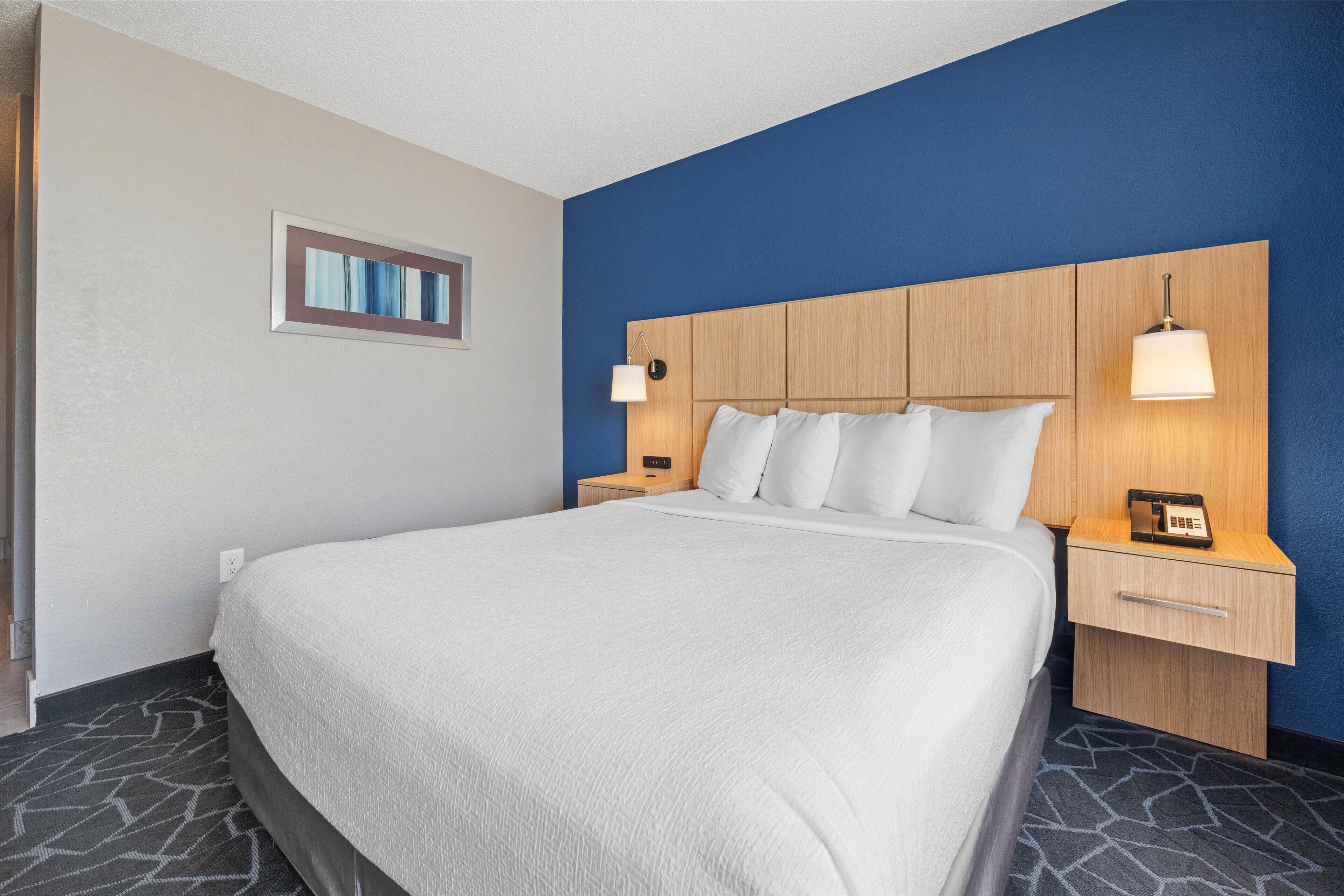 Camera d'albergo con un letto grande, una testiera in legno, due comodini con lampade e un piccolo comodino con il telefono.