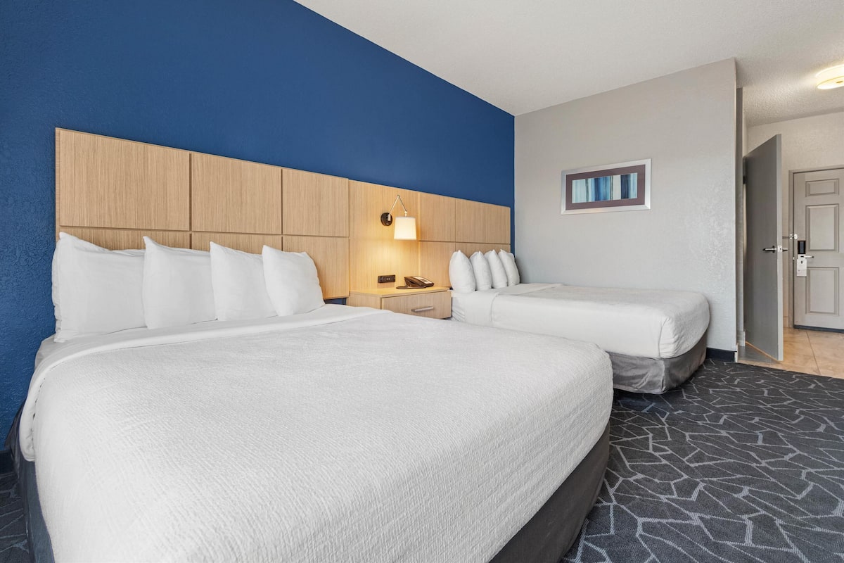 Une chambre d’hôtel avec deux lits, une tête de lit en bois, une table de chevet avec une lampe et un tableau encadré au mur.
