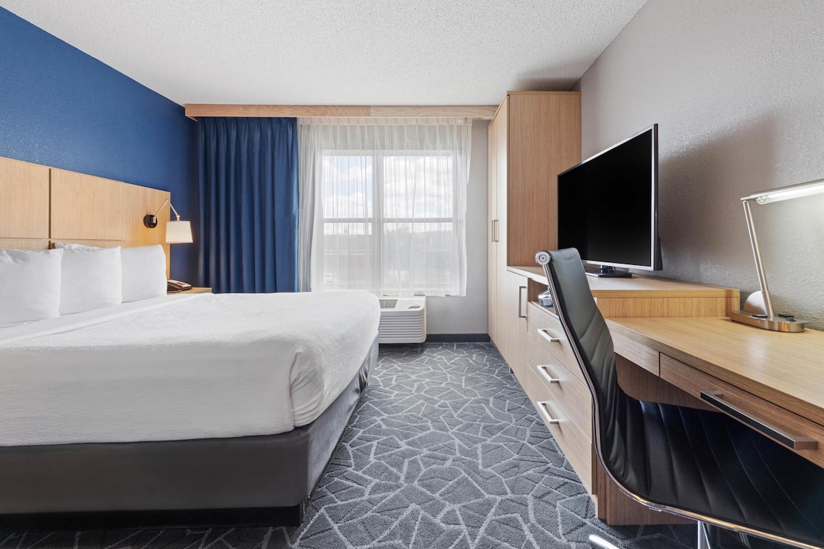 A hotel room with a bed, a desk, a TV, and a window with curtains.