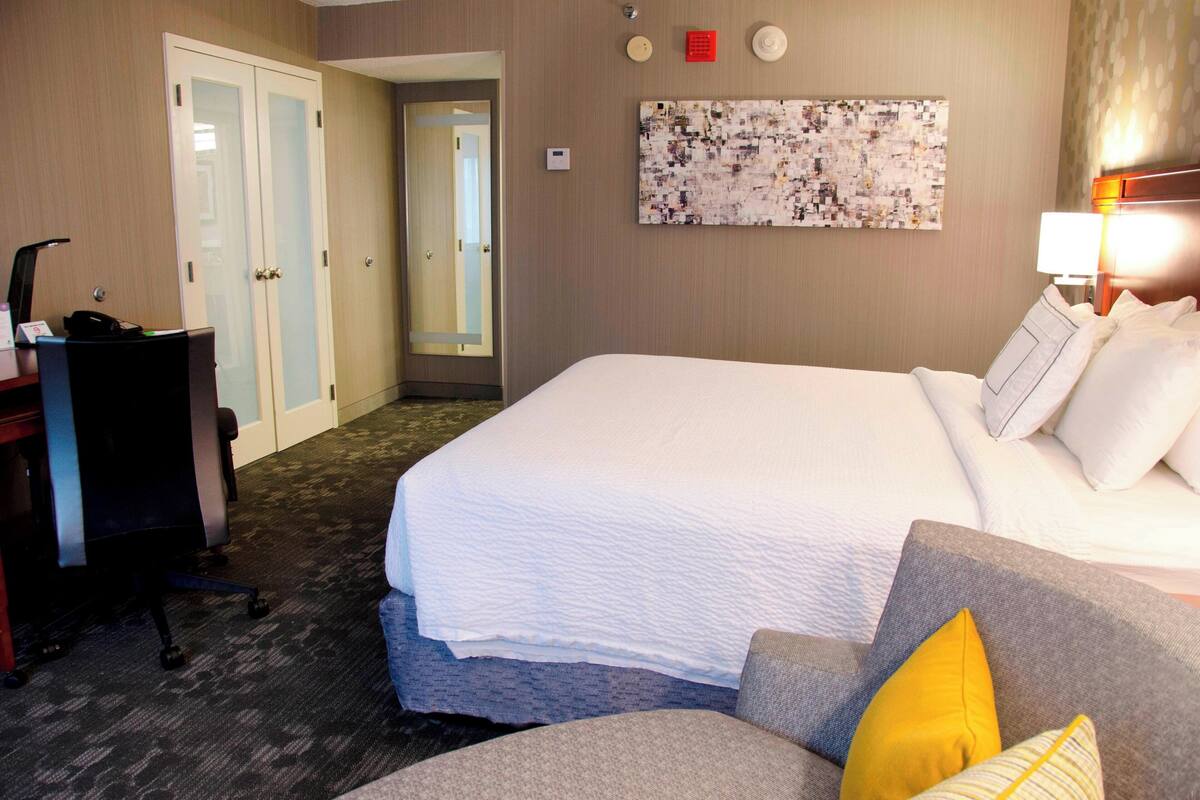 Une chambre d’hôtel avec un grand lit, un bureau avec une chaise, une lampe et une œuvre d’art accrochée au mur.