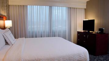 Una habitación de hotel con una cama grande, un televisor en una cómoda y una ventana con cortinas translúcidas.