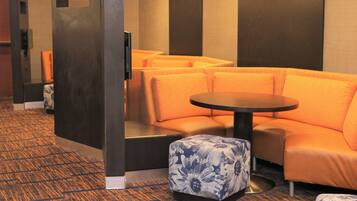 Hall dell'hotel con sedute arancioni, un tavolo rotondo e un pouf decorato.