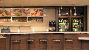 Una zona de bar con taburetes, estantes con bebidas y una máquina de café.