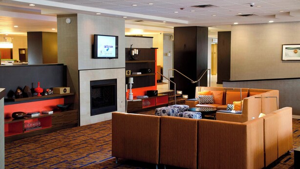 Un vestíbulo de hotel con diseño moderno, que incluye una zona de estar con sofás, una chimenea y un televisor montado en la pared.
