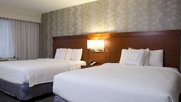 Habitación de hotel con dos camas, una mesita de noche con lámpara y un papel tapiz estampado.