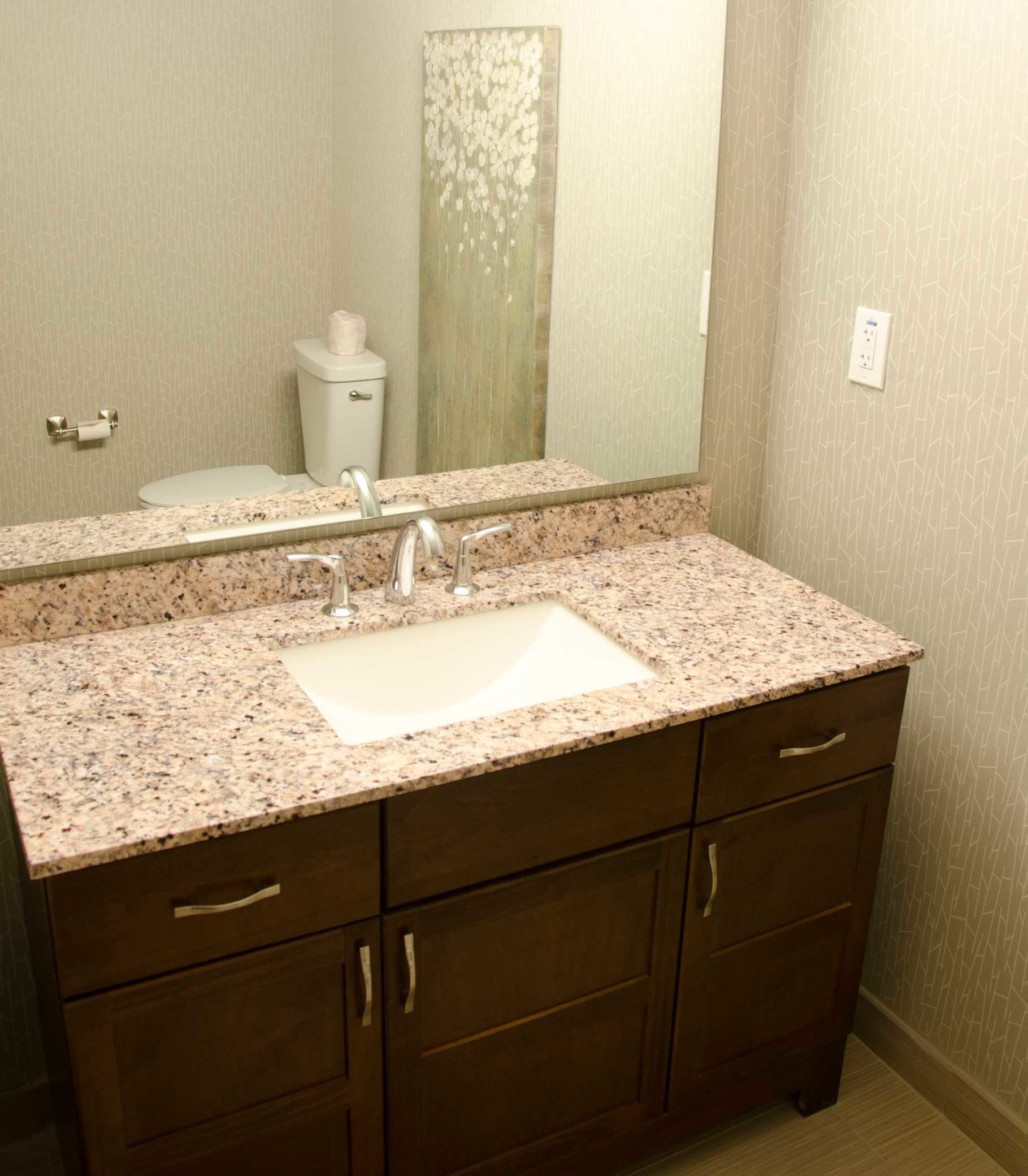 Un baño con lavamanos de encimera de granito, un espejo y armarios de madera.