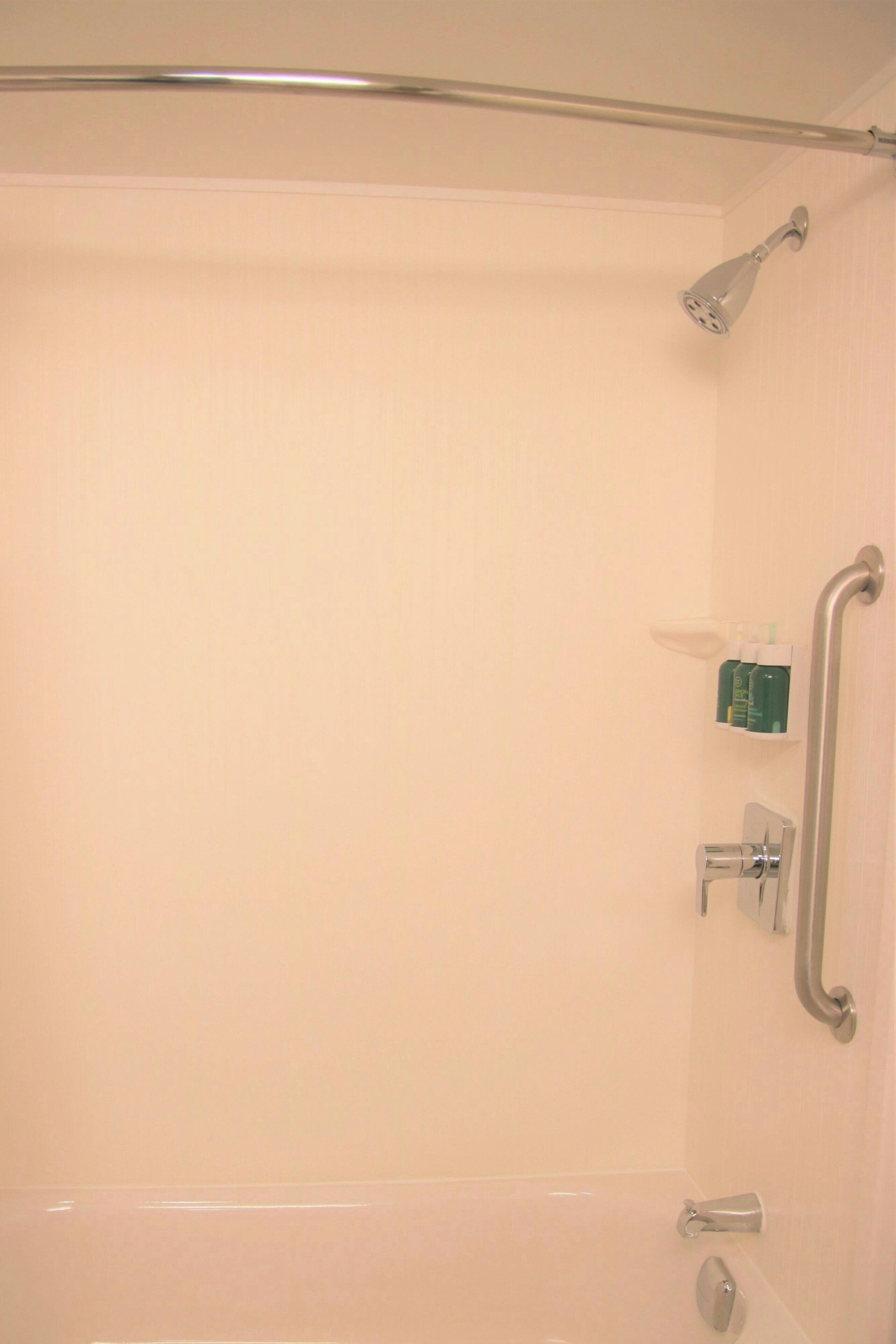 A bathroom with a shower, grab bars, and a shelf with toiletries.