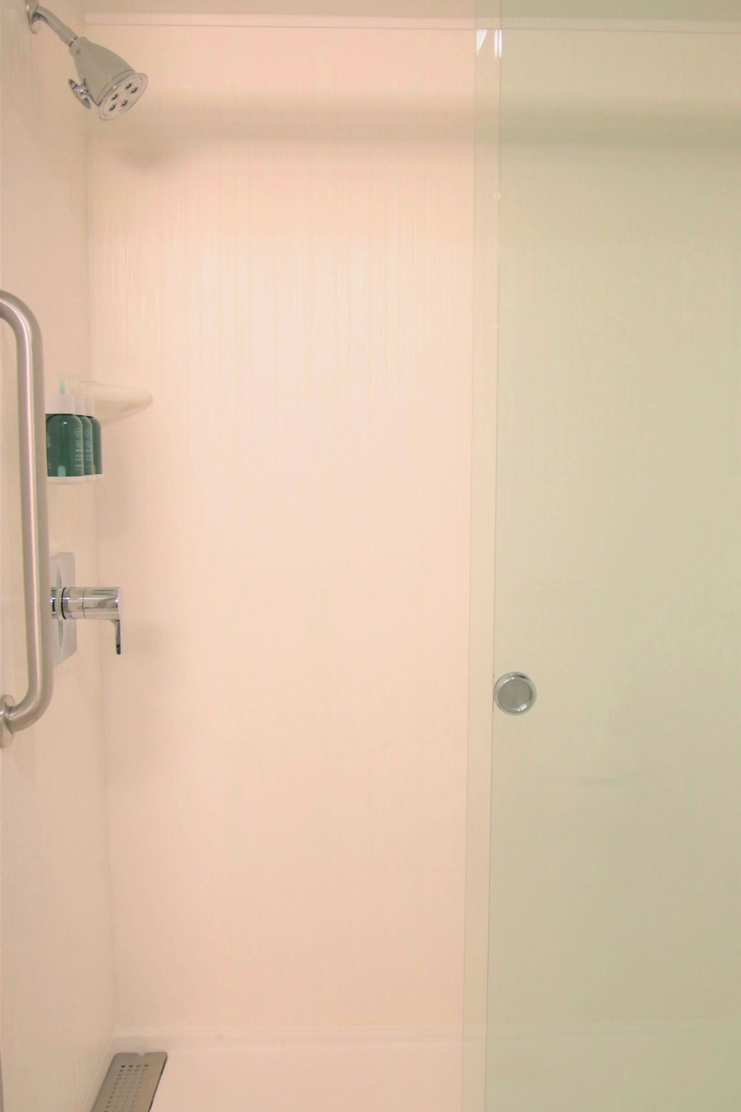 Een badkamer met een douche, handgrepen en een zeepdispenser.