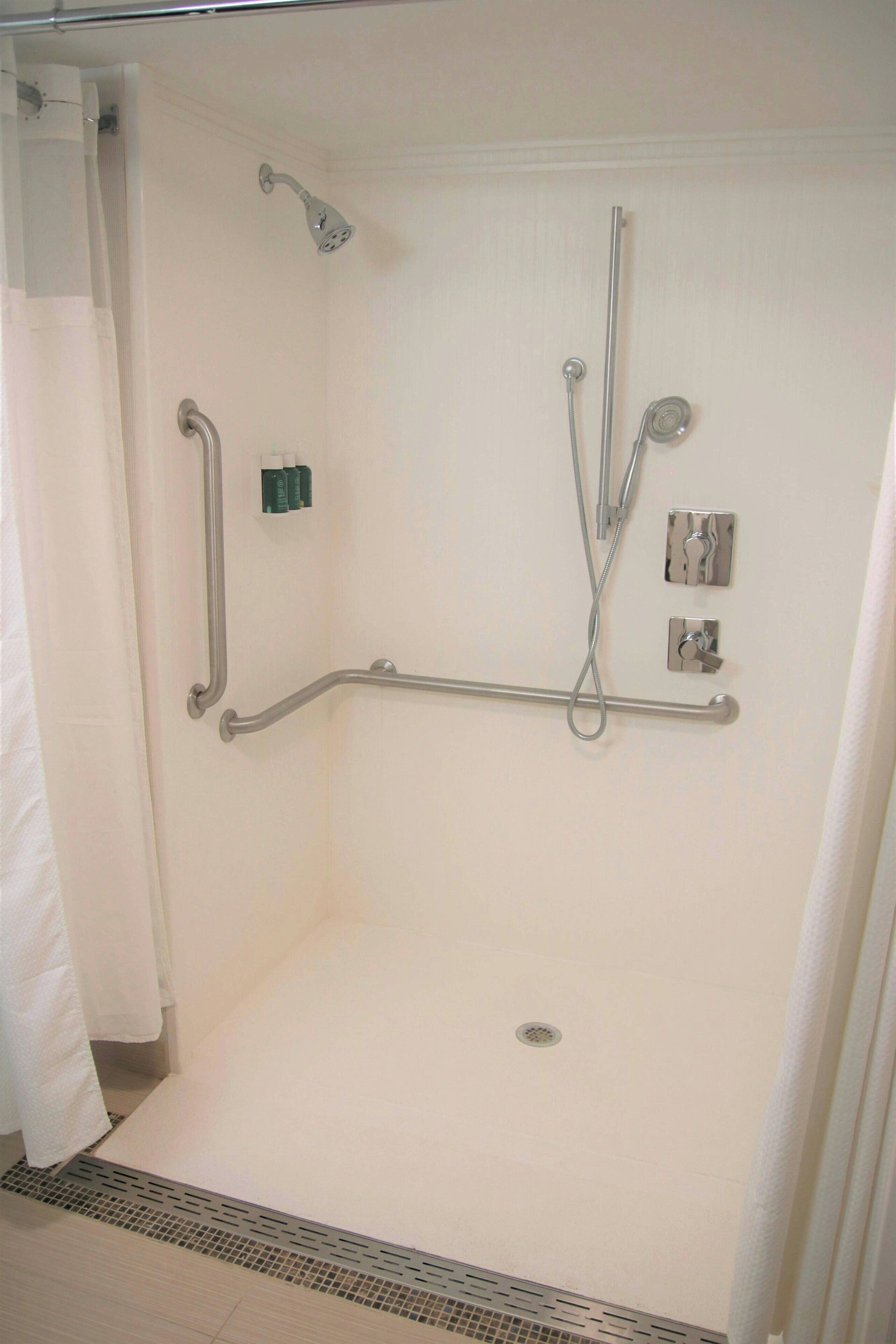 A walk-in shower with a grab bar, a handheld showerhead, and a wall-mounted control panel.