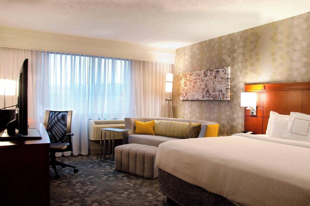 Une chambre d’hôtel avec un grand lit, un bureau avec un ordinateur, une chaise et une petite table.