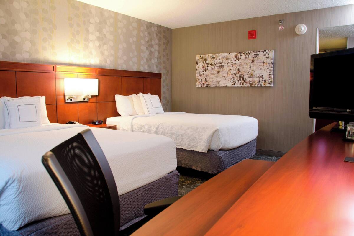 Une chambre d’hôtel avec deux lits, une tête de lit en bois, un téléviseur à écran plat et une œuvre d’art accrochée au mur.