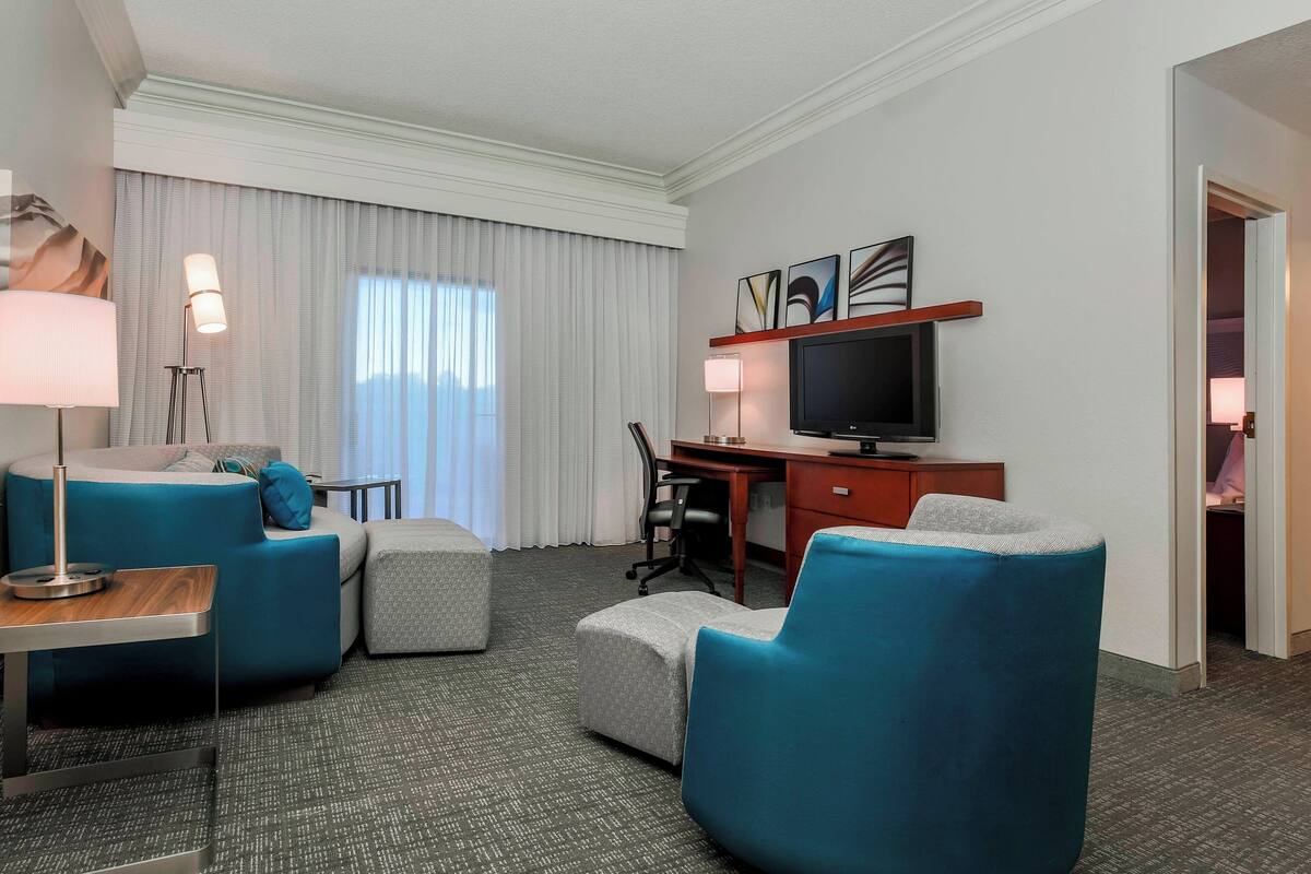 A hotel room with a desk, a TV, a sofa, and a chair.