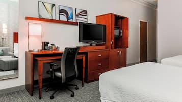 Una habitación de hotel con un escritorio de madera, un televisor, una cama y un armario.