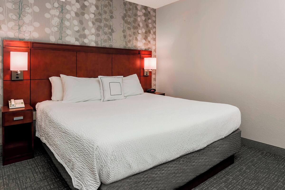 A hotel room with a large bed, two bedside tables, a nightstand, and a wall with a leaf pattern.