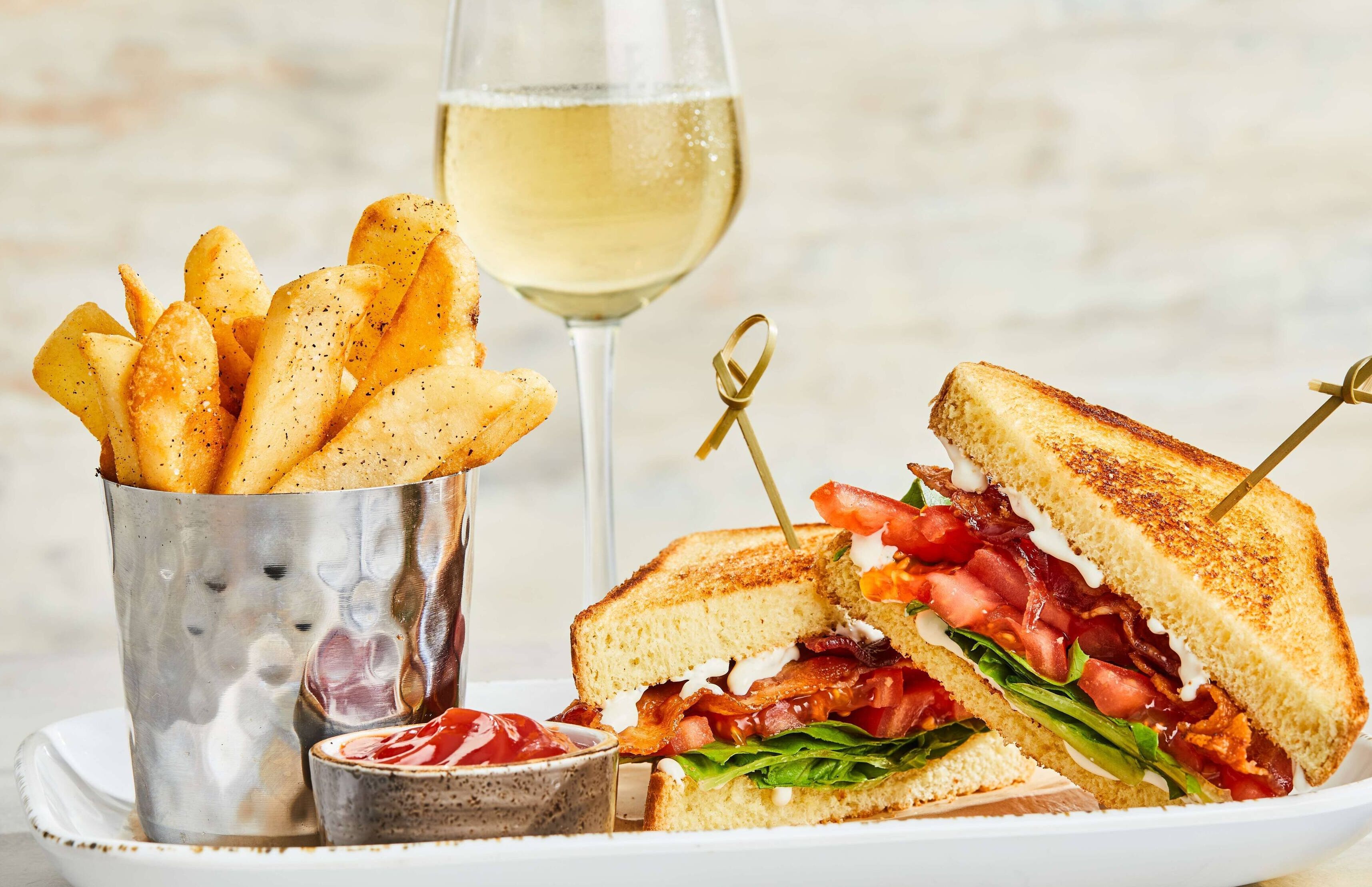 A sandwich with a side of fries and a glass of white wine.