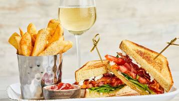 Un plato con un sándwich a la parrilla, una copa de vino blanco y un recipiente con papas fritas sazonadas.