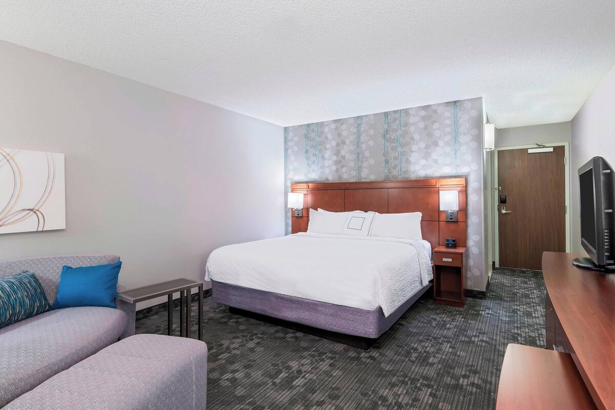 Quarto de hotel com uma cama grande, uma escrivaninha, uma cadeira, um sofá e uma televisão.