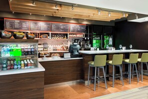 A modern bar area with a wooden counter, stools, a menu board, and a refrigerated display of beverages. - Courtyard by Marriott Sarasota Bradenton Airport (Sarasota)
