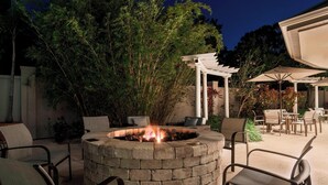A circular fire pit with seating around it, surrounded by trees and outdoor furniture.