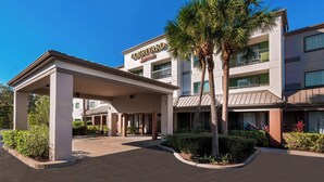 A Courtyard Marriott hotel with a covered entrance, palm trees, and a clear blue sky.