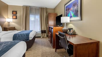 A hotel room with two beds, a desk, a chair, a television, and a framed picture on the wall.