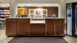 A hotel reception desk with a sign reading "Comfort Inn & Suites," a self-service kiosk, and a snack bar in the background. - Comfort Inn & Suites Hamilton Place (Chattanooga)