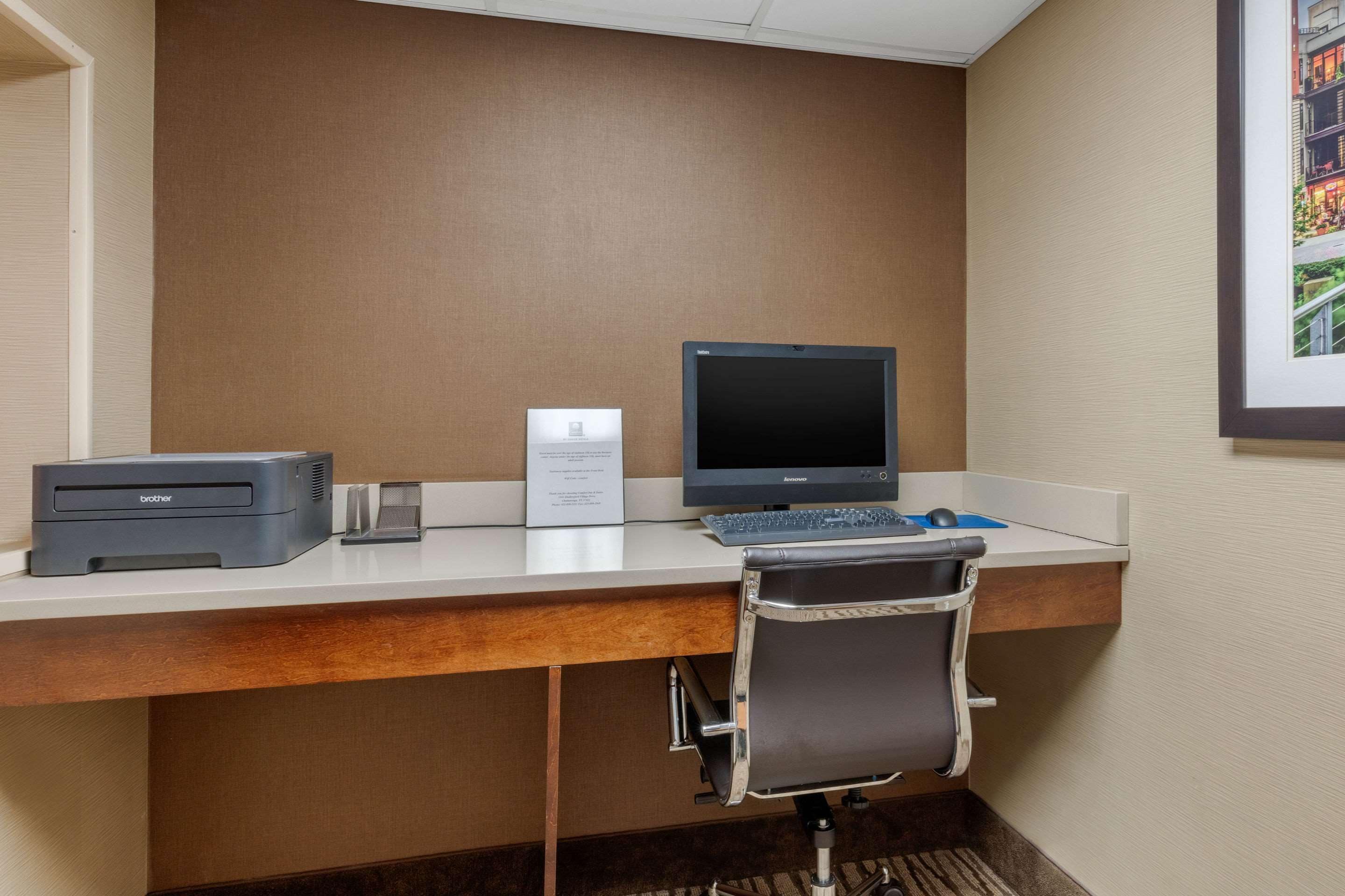 A hotel workspace with a desk, a Brother printer, a Brother scanner, a Brother monitor, and a chair.