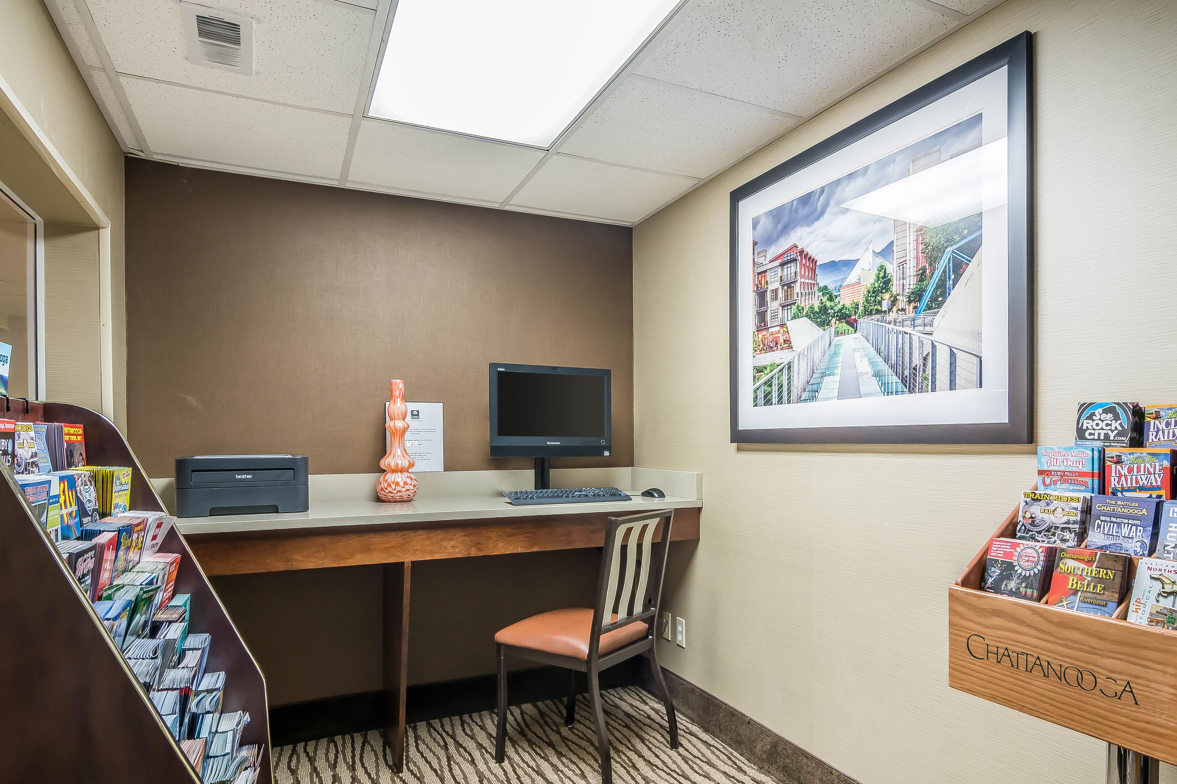 A hotel room with a desk, computer, chair, and a wall-mounted TV.