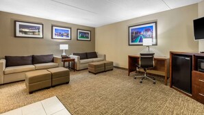 A hotel room with a sofa, two ottomans, a desk with a chair, a TV, and framed pictures on the walls. - Comfort Inn & Suites Hamilton Place (Chattanooga)