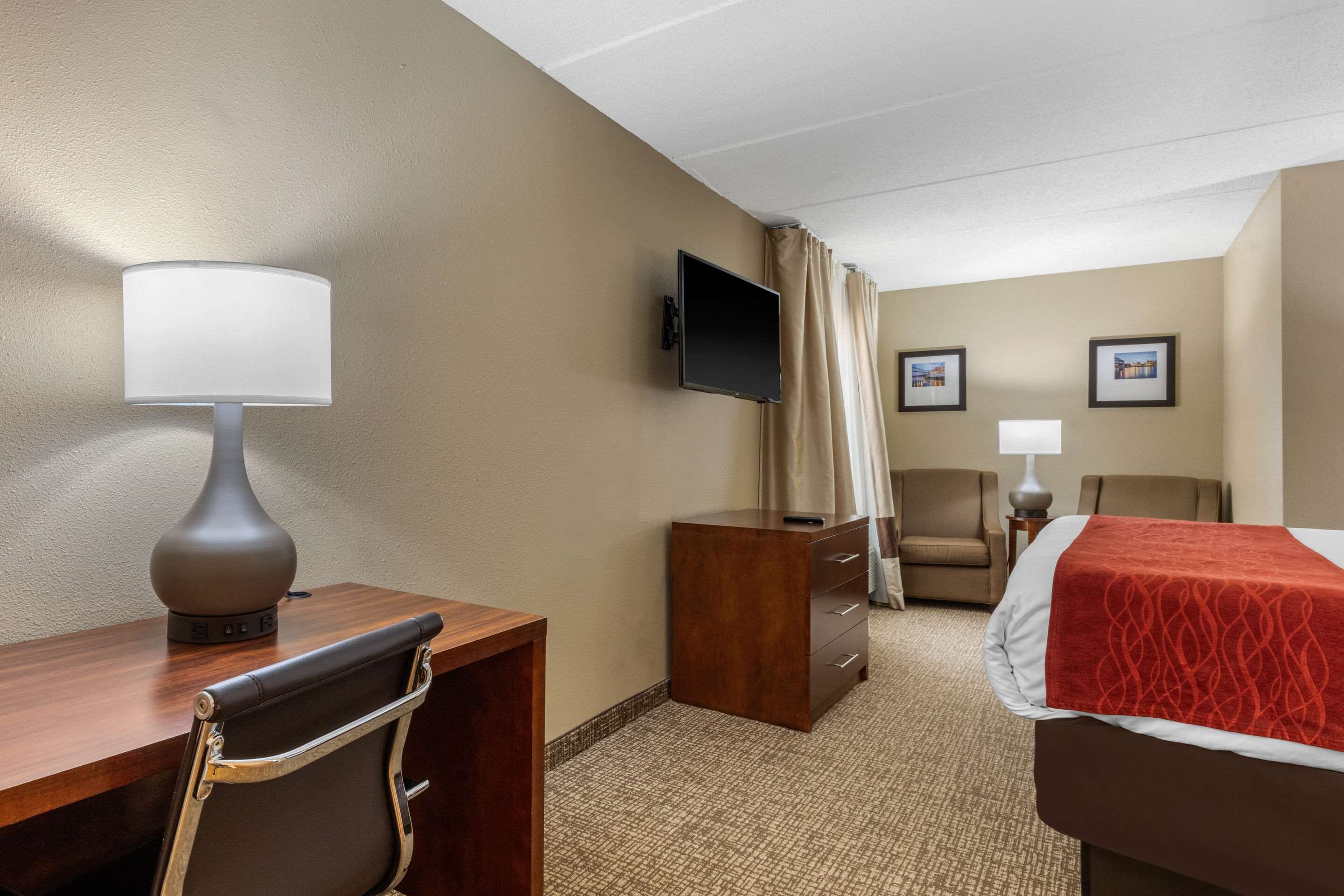 Habitación de hotel con escritorio, silla, cama, televisor y dos cuadros en la pared.