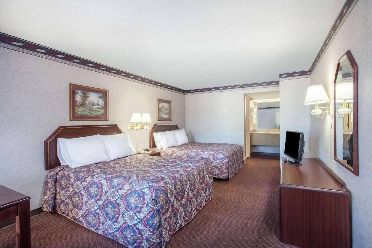 A hotel room with two beds, a TV, a desk, and a mirror.