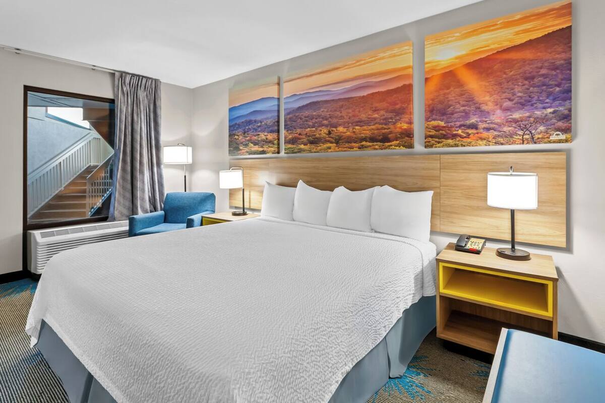 A hotel room with a large bed, two bedside tables with lamps, a blue chair, and a view of a staircase.