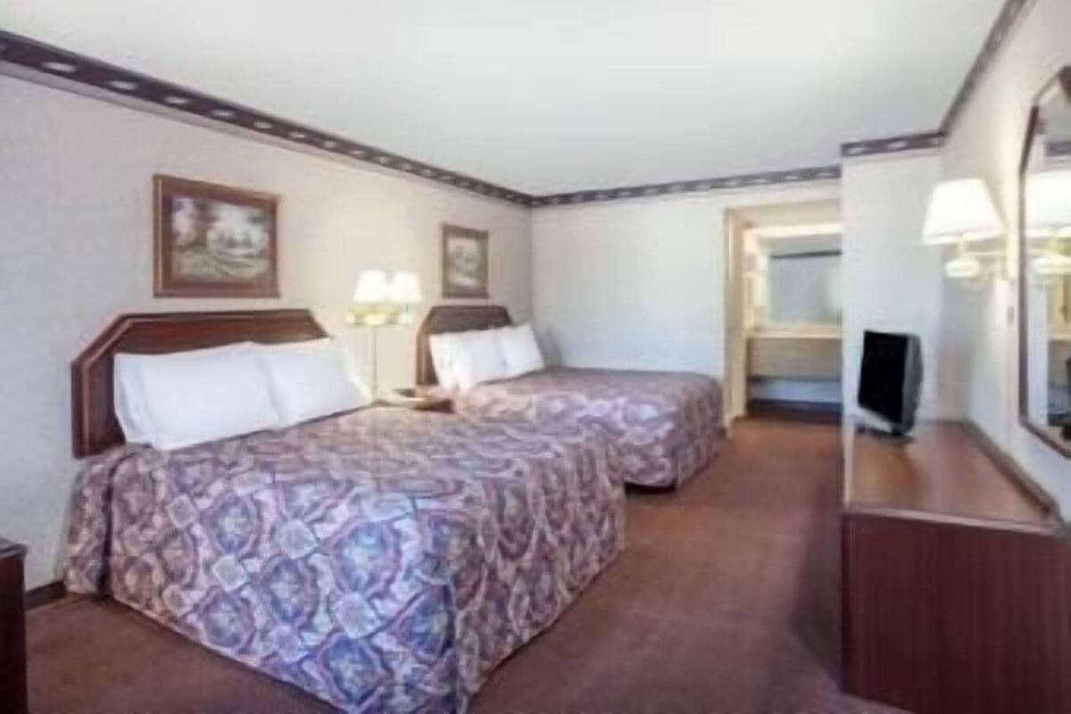 A hotel room with two beds, a TV, and a mirror.