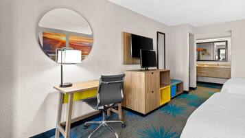 A hotel room with a desk, chair, bed, and a round mirror.