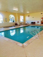 An indoor swimming pool with clear water, surrounded by lounge chairs and a tiled floor.