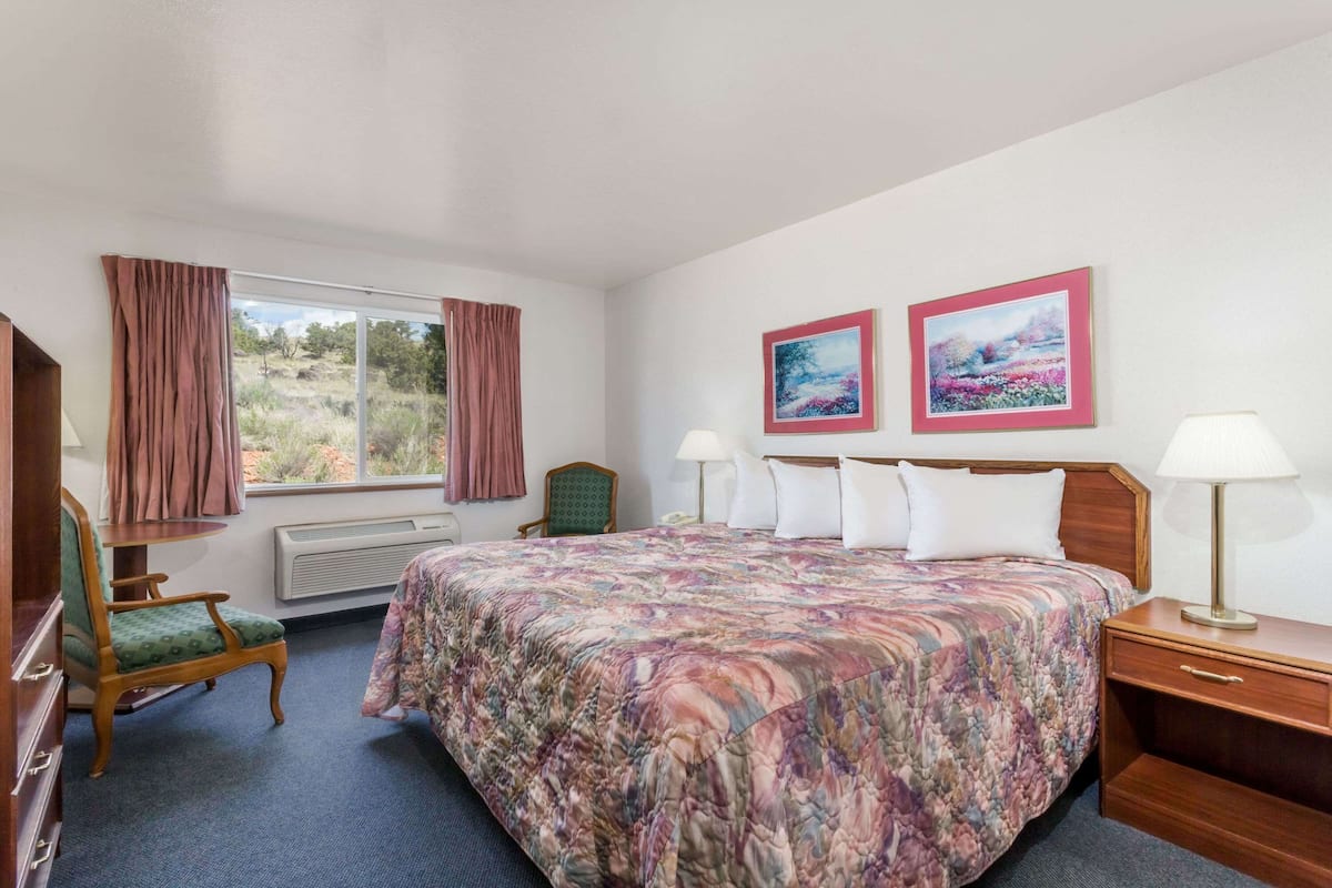 Ein Hotelzimmer mit einem großen Bett, zwei Nachttischlampen, einem Sessel, einem Schreibtisch und zwei gerahmten Bildern an der Wand.