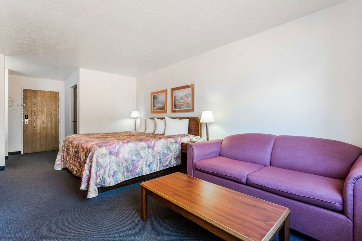 Ein Hotelzimmer mit einem Bett, einem violetten Sofa, einem Holztisch und zwei Nachttischlampen sowie einer Tür.