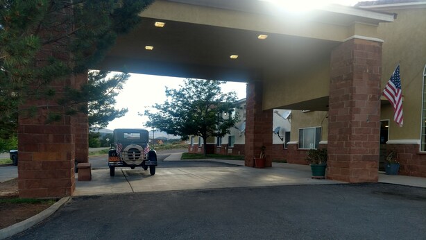 A building entrance with a vintage car parked under a covered area, American flags, and potted plants.